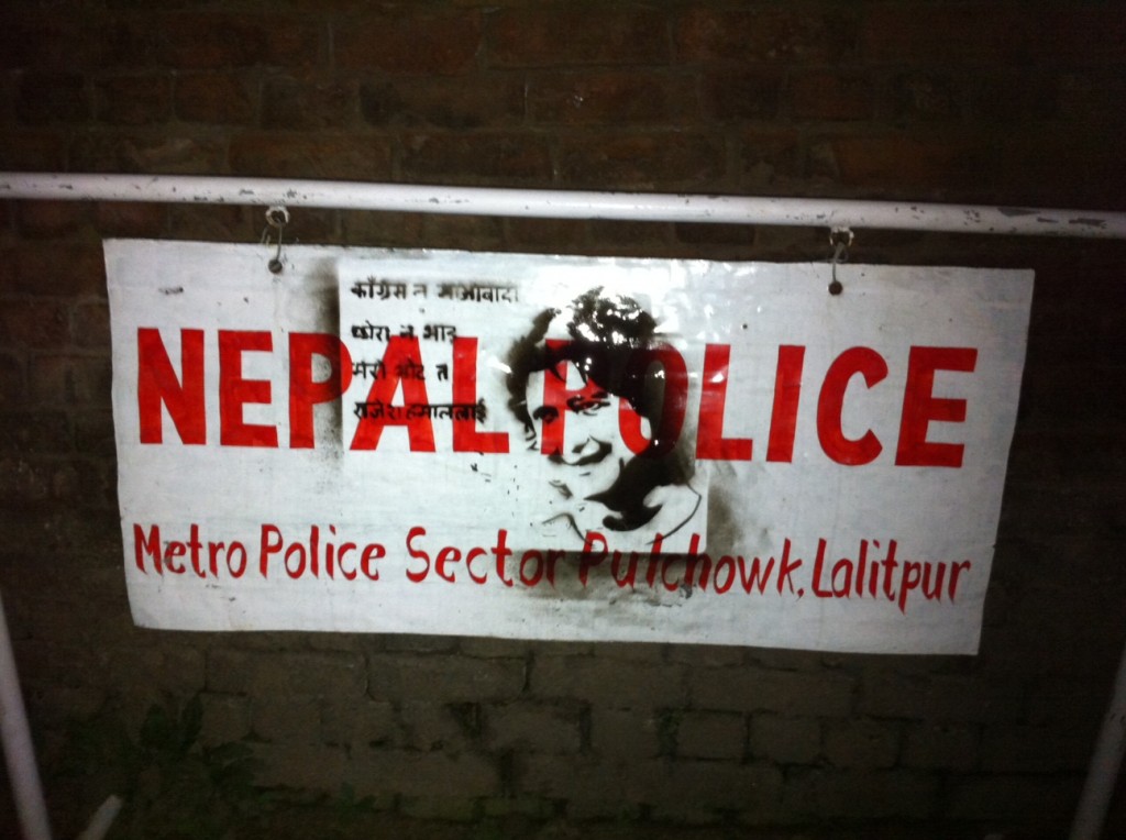 a graffiti of a faux political campaign slogan (in Nepali), along with the face of the Nepalese actor Rajesh Hamal, on a metal barricade with 'Nepal Police' written on it (in English)
